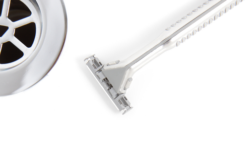 Close-up of a metallic safety razor and part of a circular drain on a white background.